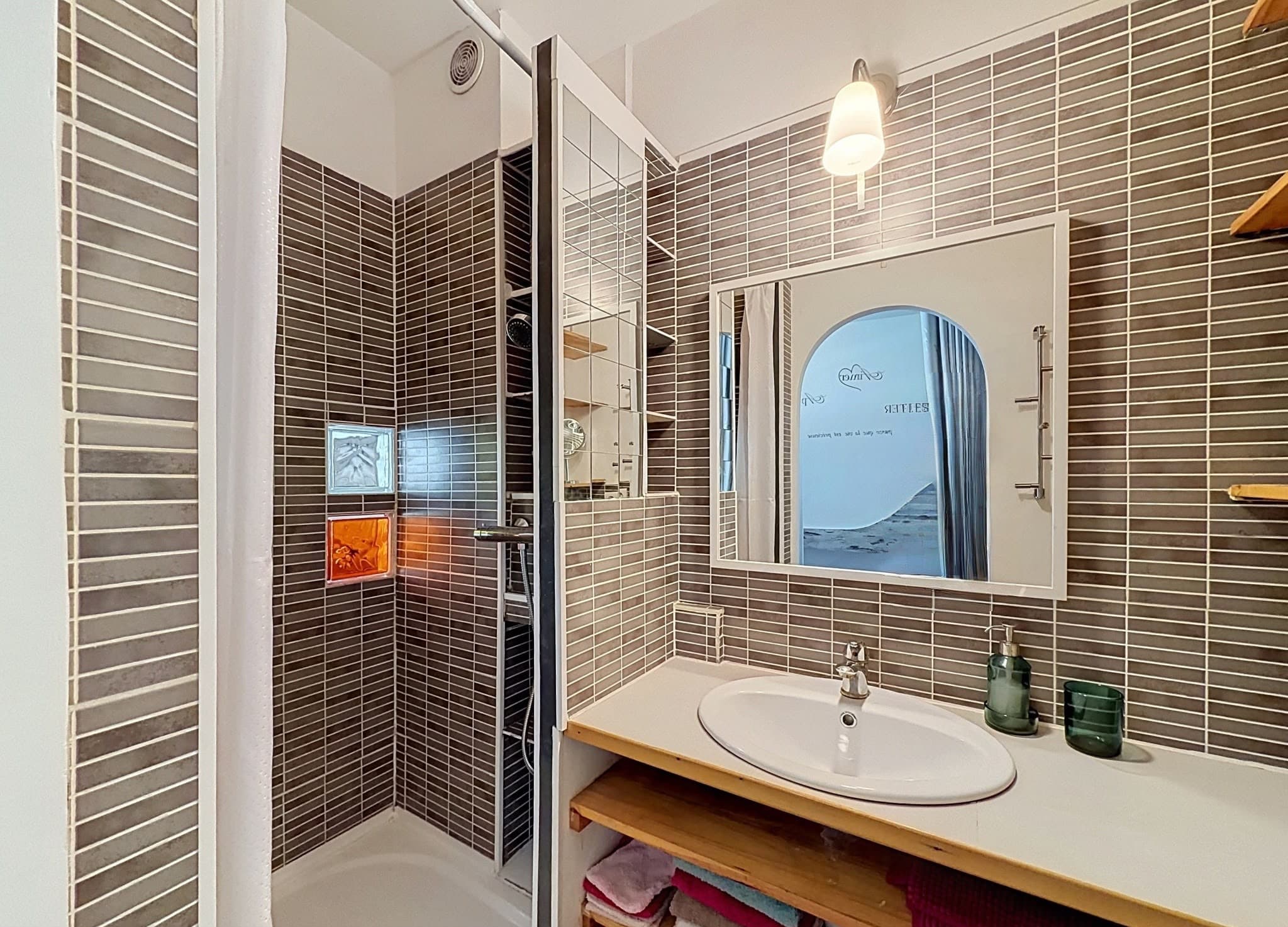 La douche carrelée de la salle d'eau, le lavabo et son grand miroir